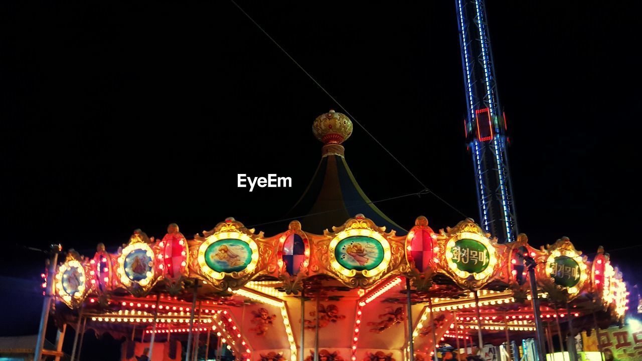 LOW ANGLE VIEW OF ILLUMINATED CAROUSEL AT NIGHT