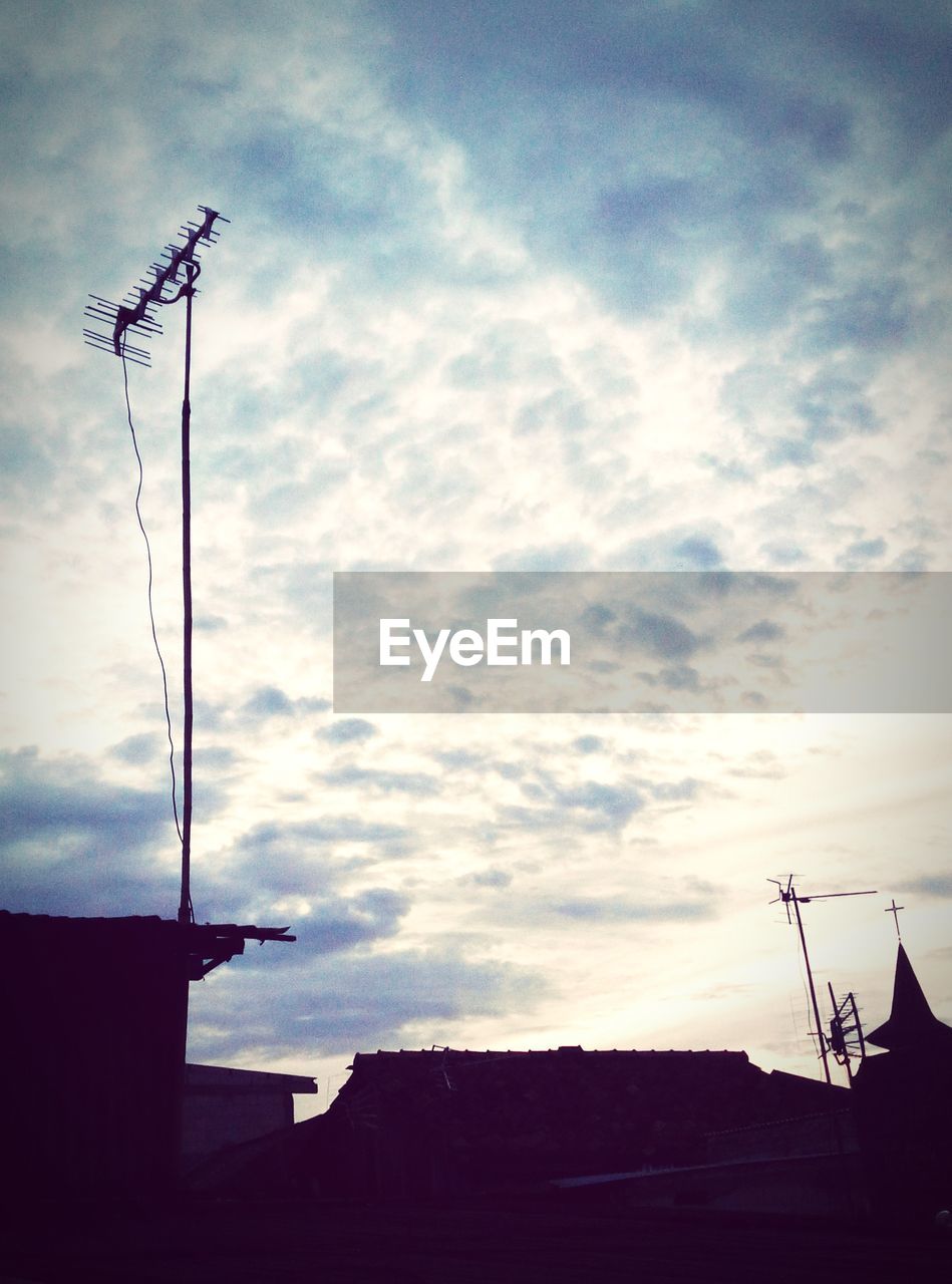 Silhouette of houses with antennas against cloudy sky