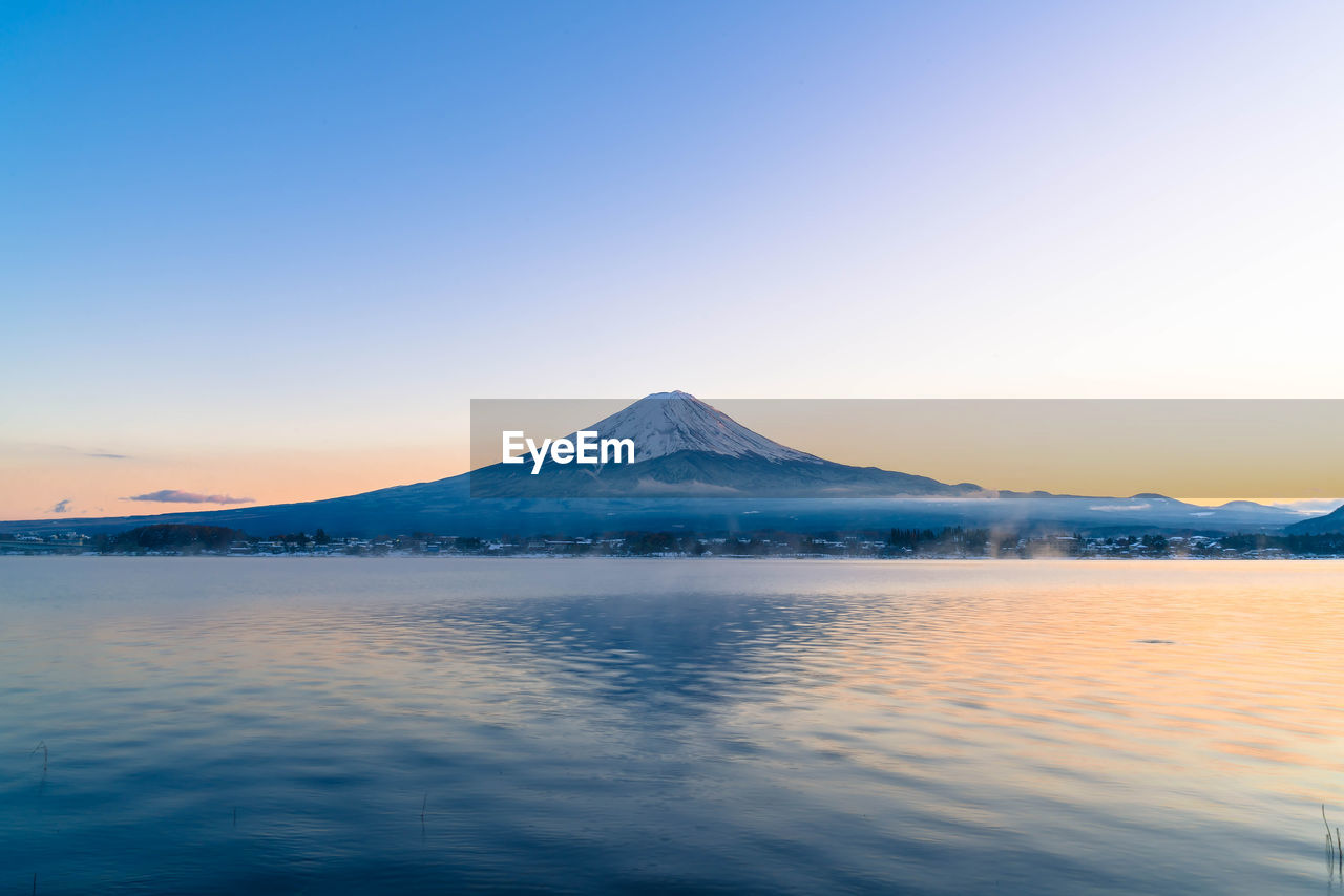 SCENIC VIEW OF LAKE BY SNOWCAPPED MOUNTAINS AGAINST SKY AT SUNSET