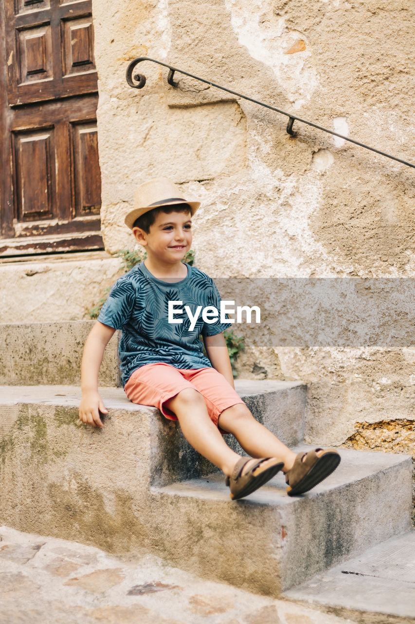 Full length of cute boy wearing hat sitting on steps