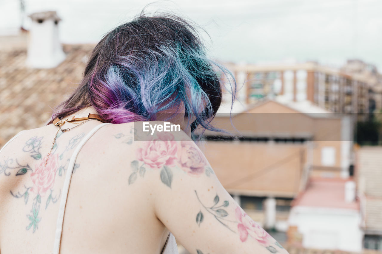 Rear view of woman with tattoo against buildings and sky