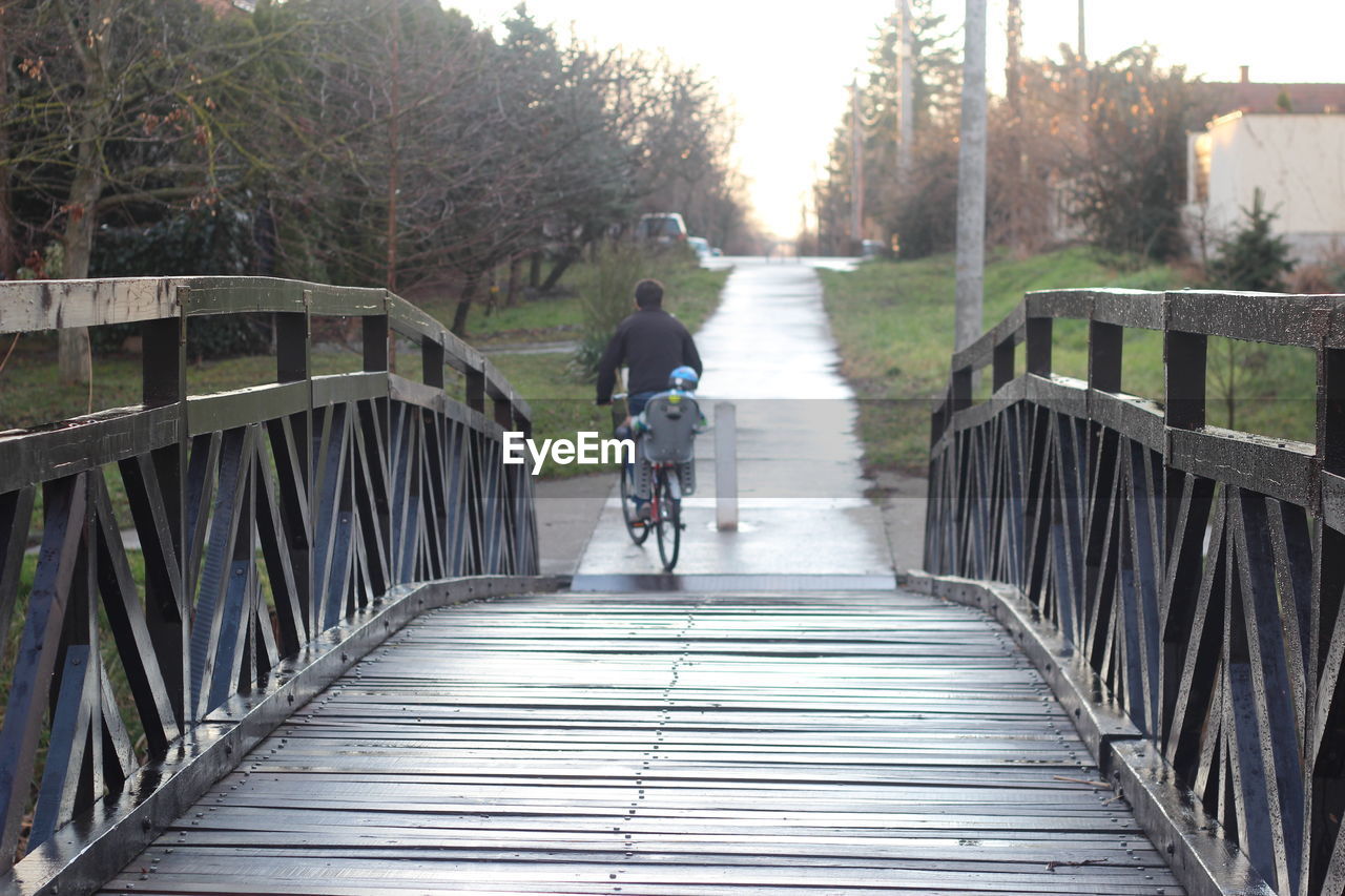 REAR VIEW OF MAN RIDING BICYCLE AGAINST SKY