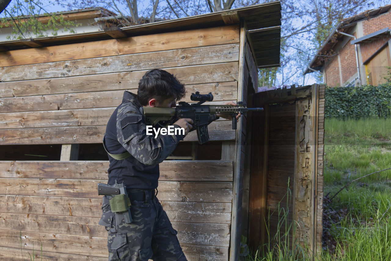 A young sniper aims at a house from the woods