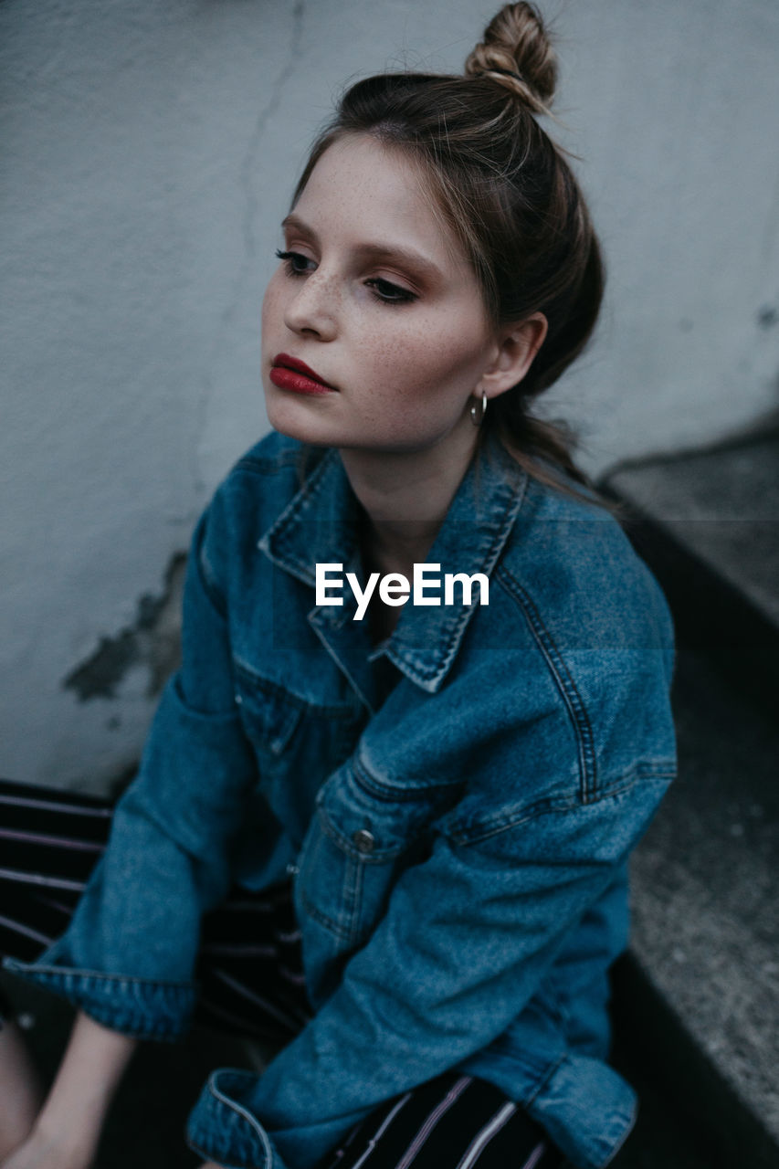 Thoughtful woman wearing denim jacket while sitting outdoors