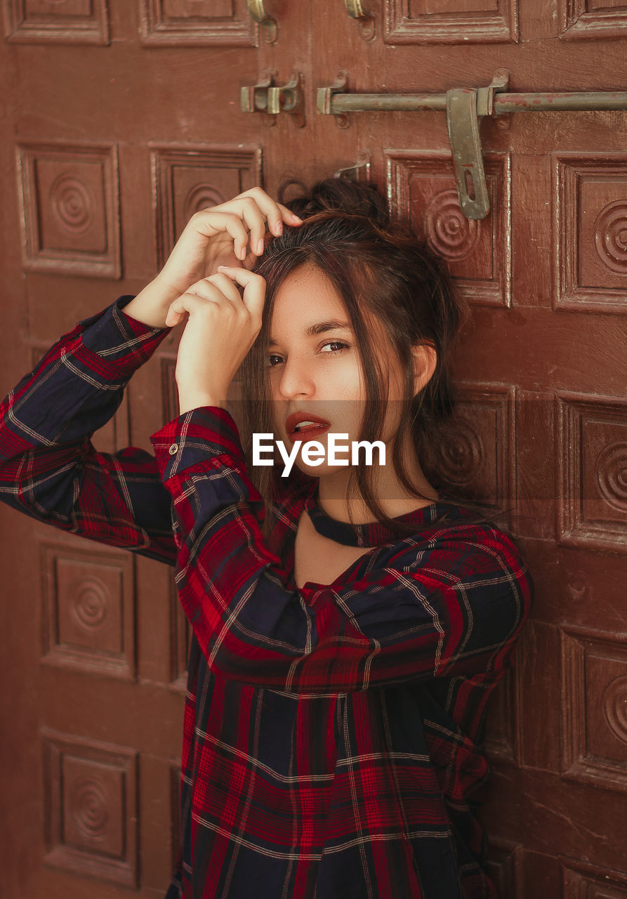 Young woman standing by wooden door