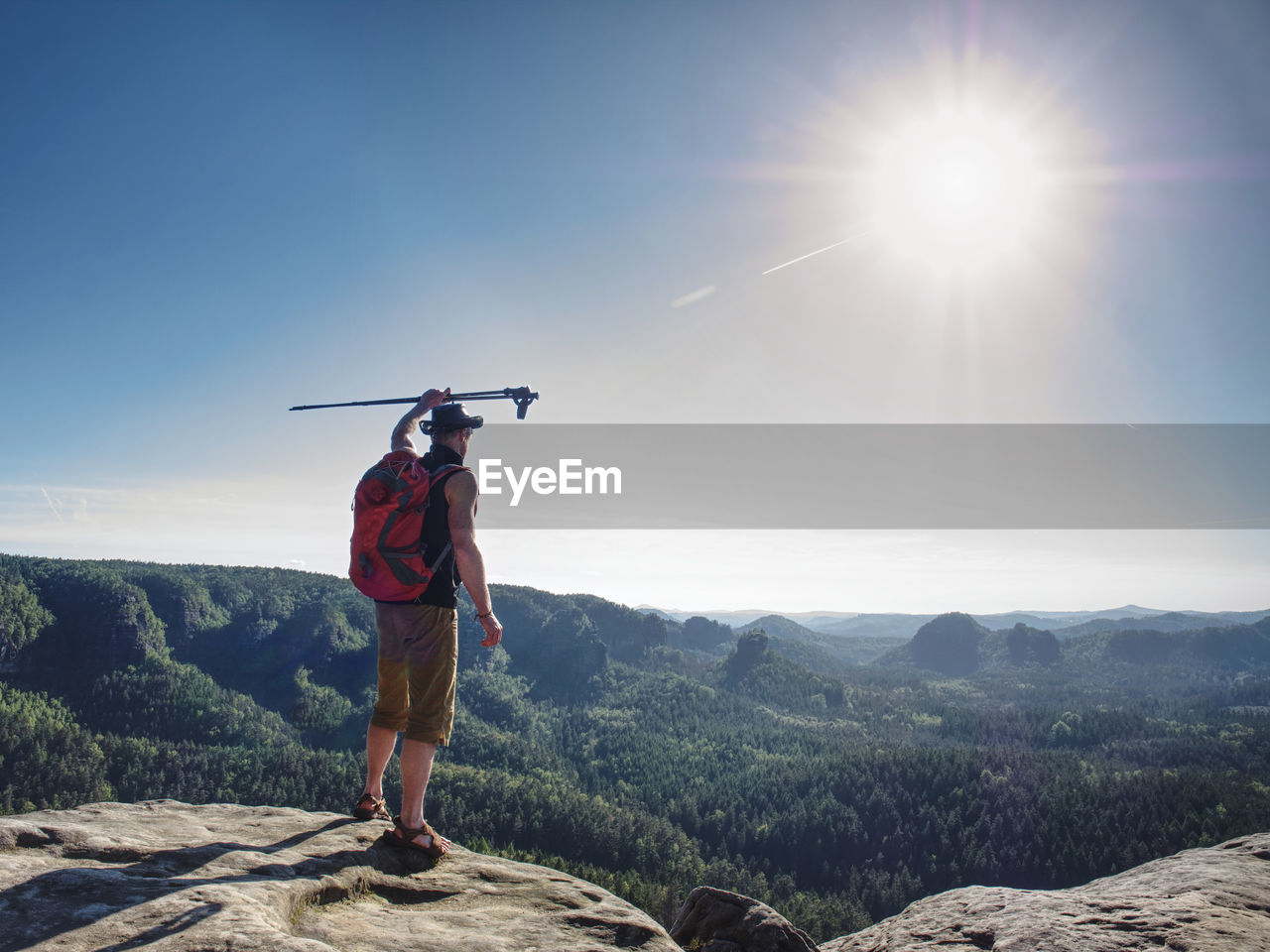 Hiker with red backpack greetings the world with arm rised up head with trekking stick. man alone