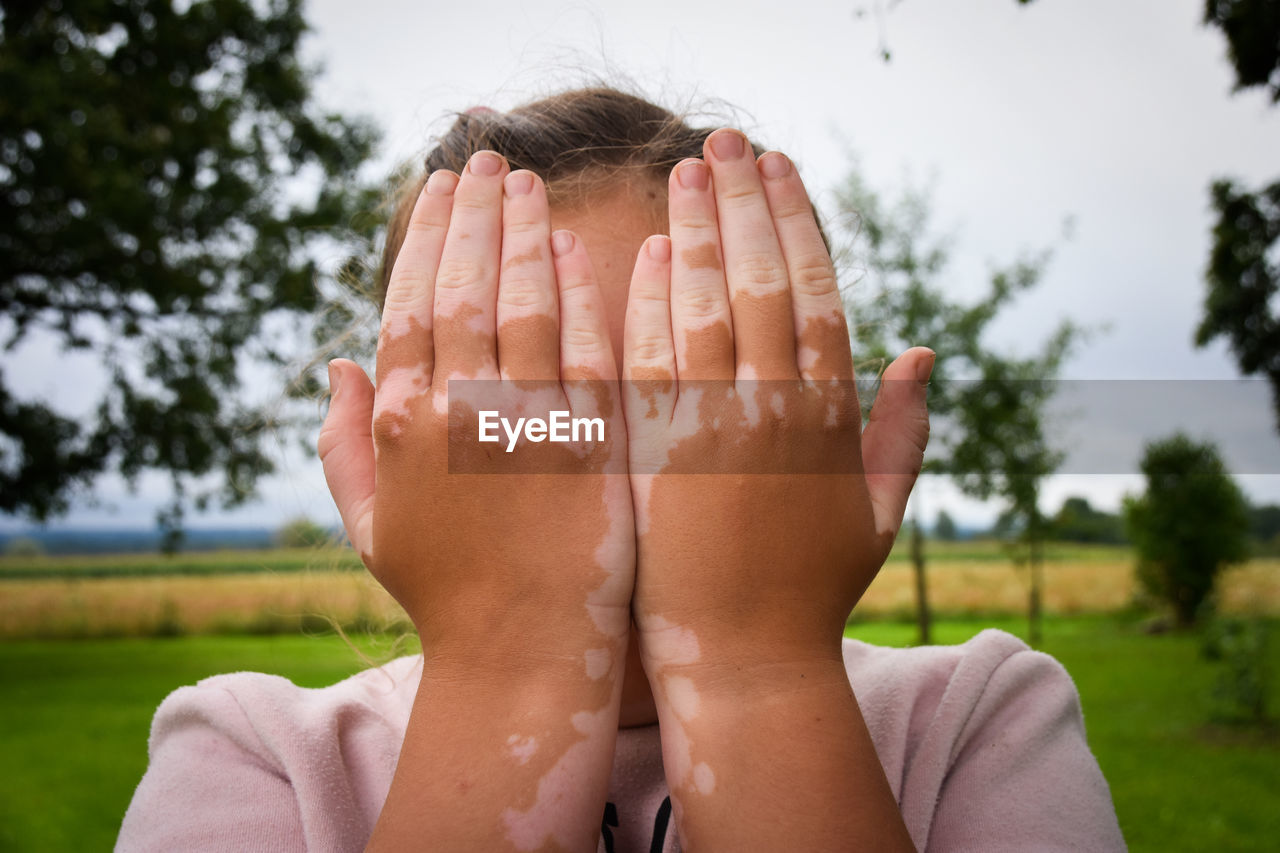 CLOSE-UP OF HUMAN HAND ON FIELD AGAINST SKY