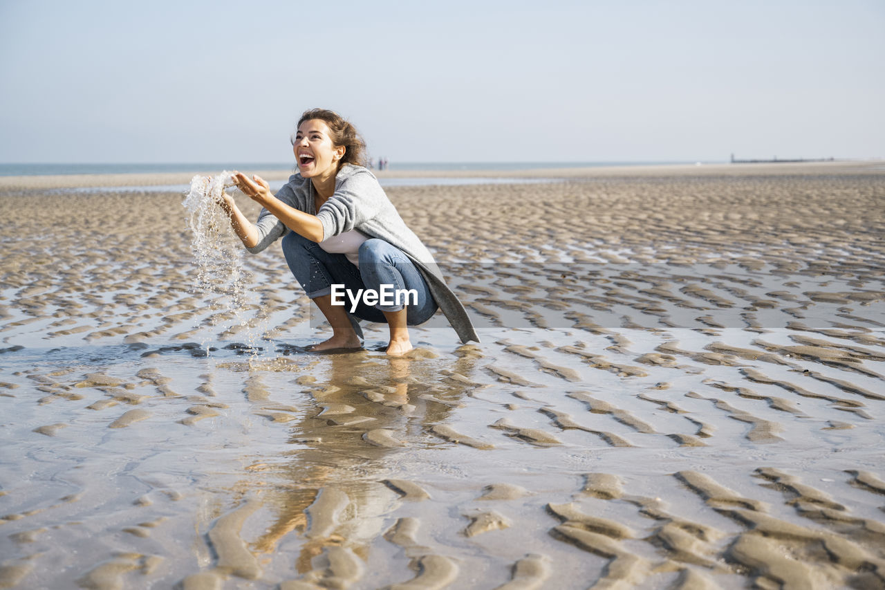 Cheerful young woman playing with water at seashore