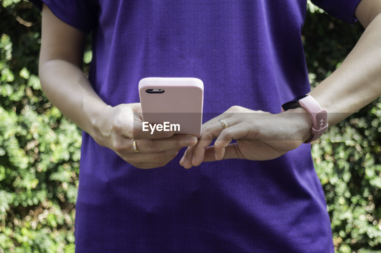 MIDSECTION OF MAN HOLDING SMART PHONE ON PURPLE MOBILE