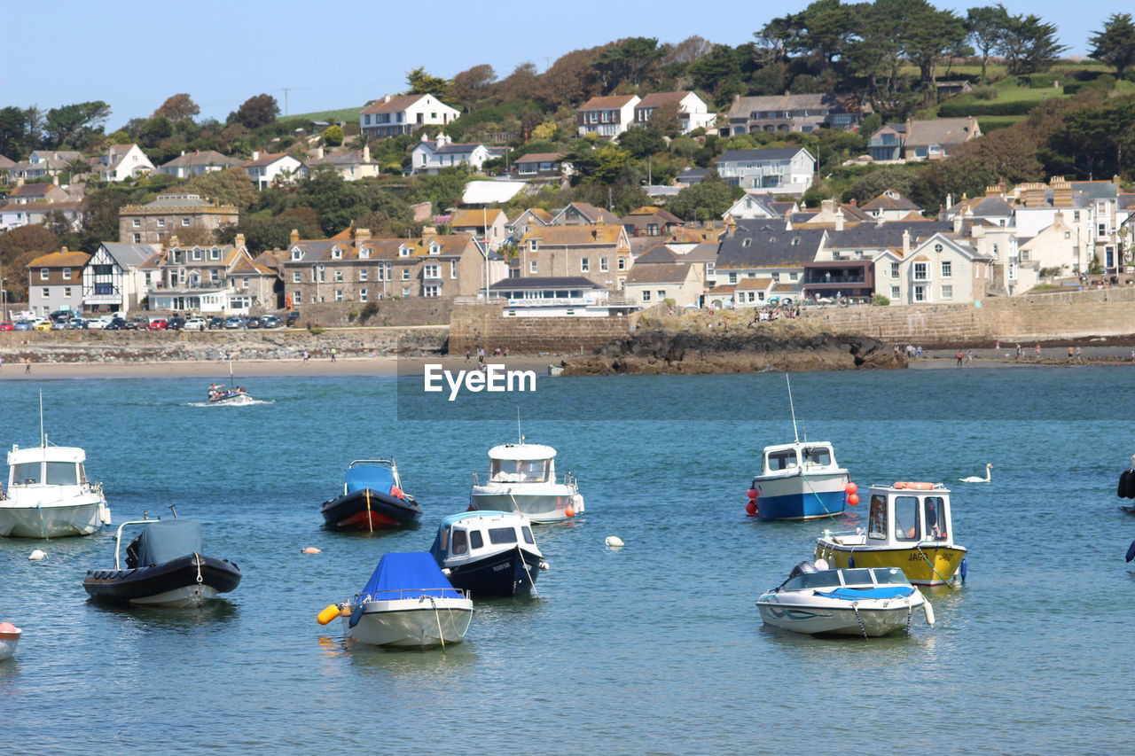 SAILBOATS MOORED ON SEA BY TOWNSCAPE