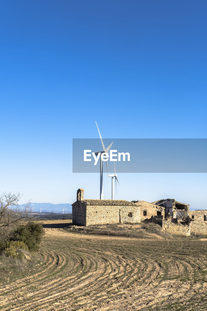 Wind turbines in between agricultural fields and an abandoned old town in catalonia spain