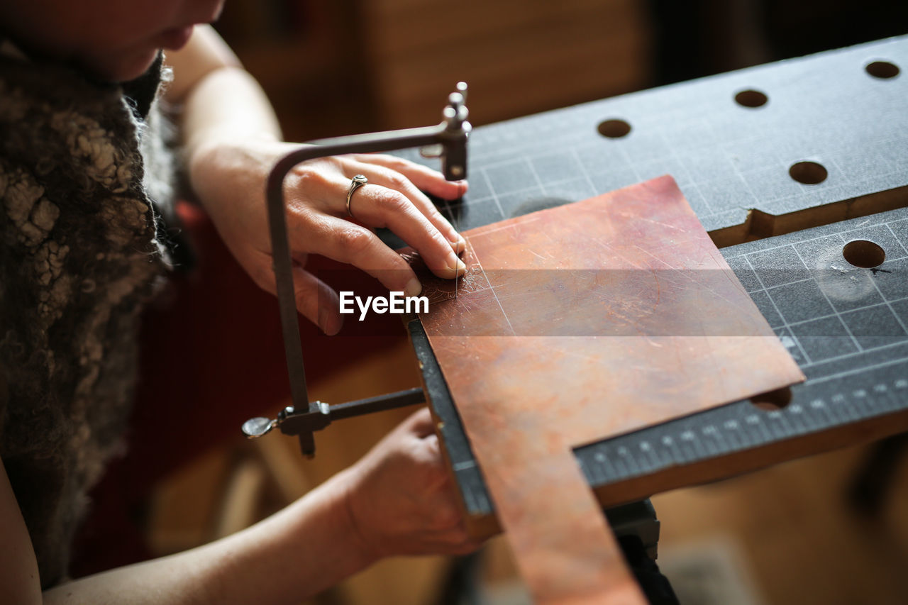 Master in the home workshop saws out a piece of copper metal with a jigsaw, concept creativity 