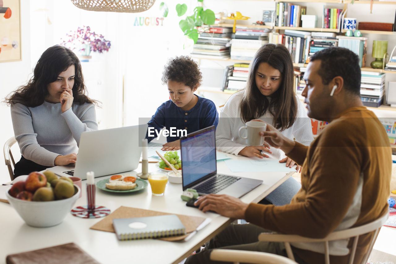 Parents working on laptop while sitting with son and daughter at table