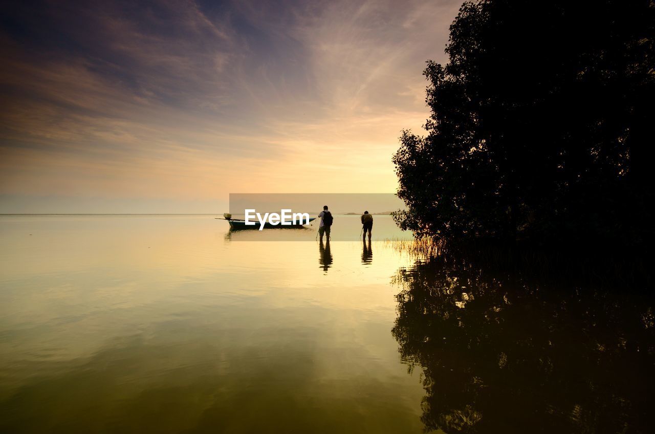 Silhouette people on shore against sky during sunset