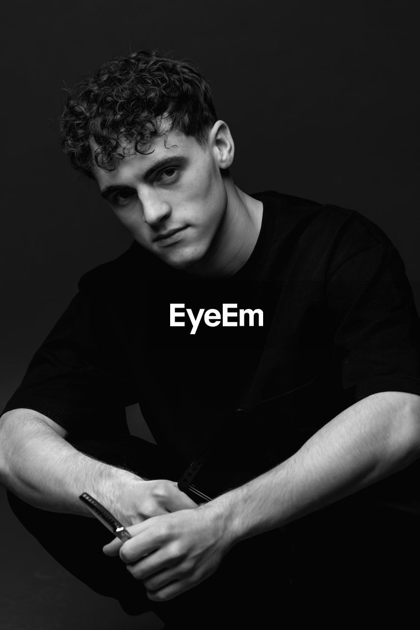 Portrait of young man sitting against black background