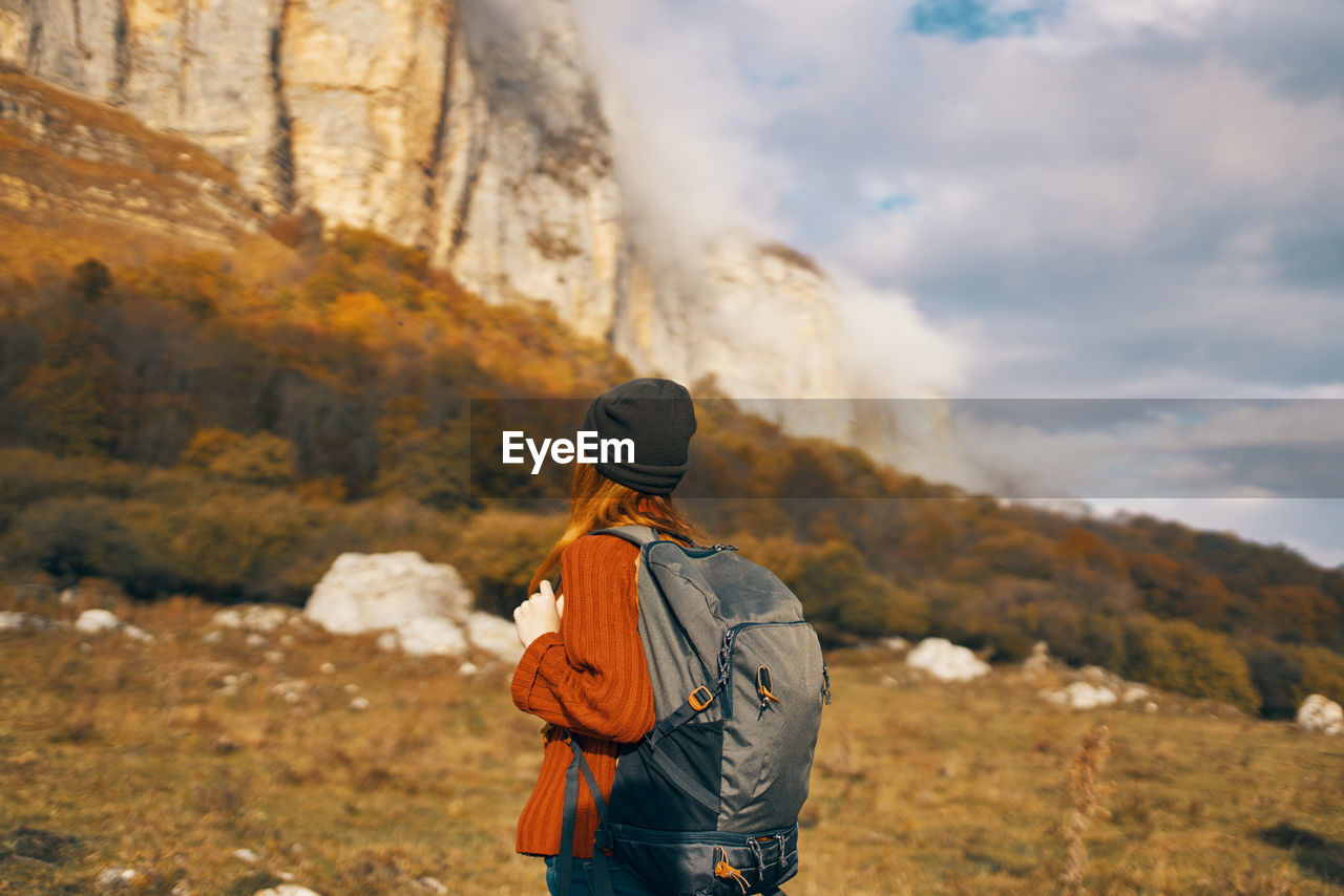 REAR VIEW OF MAN STANDING AGAINST MOUNTAINS