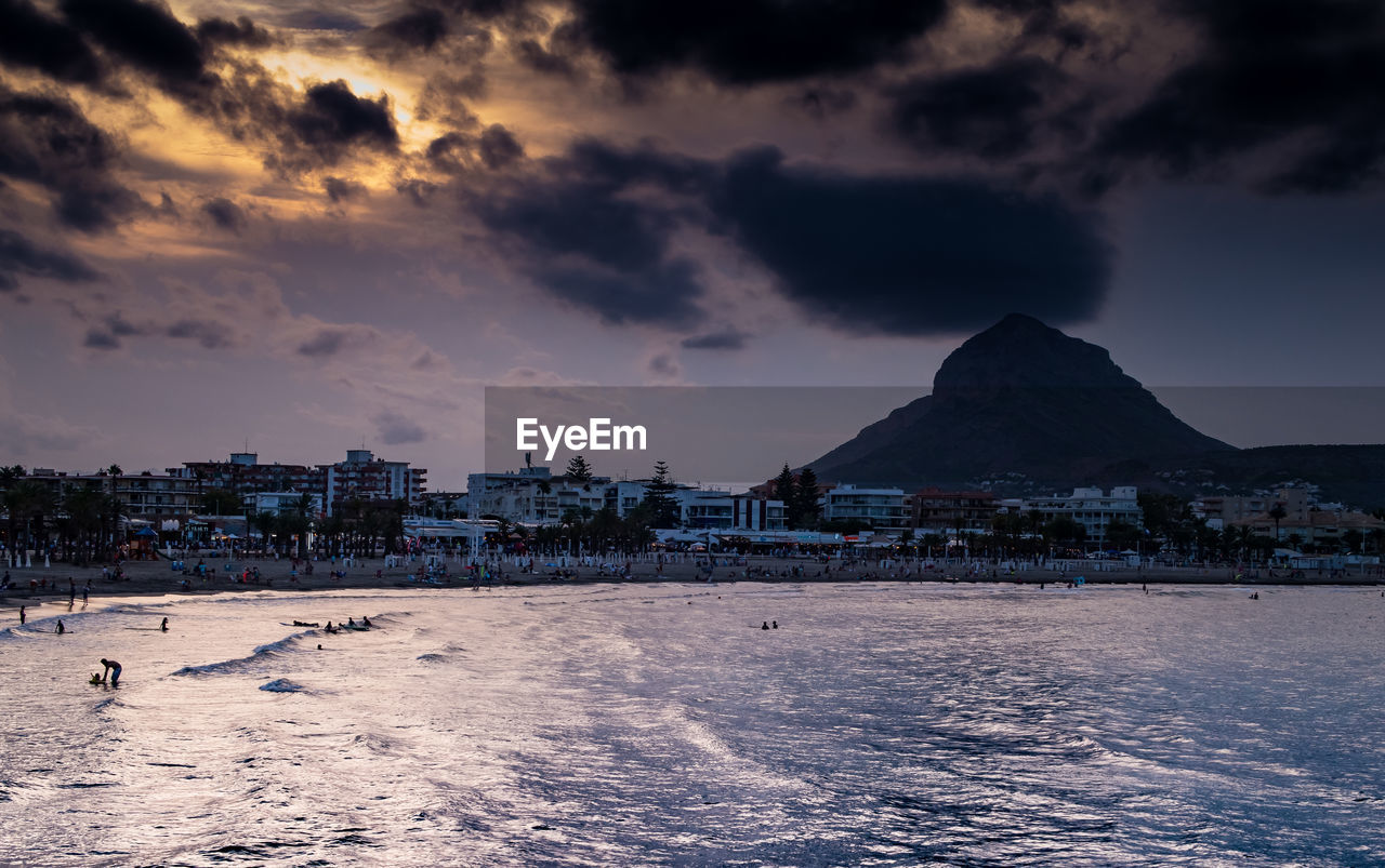 BUILDINGS BY SEA AGAINST SKY DURING SUNSET