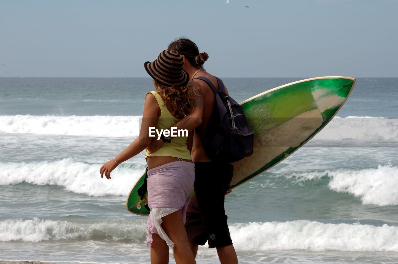 Man carrying surfboard while walking with woman at beach