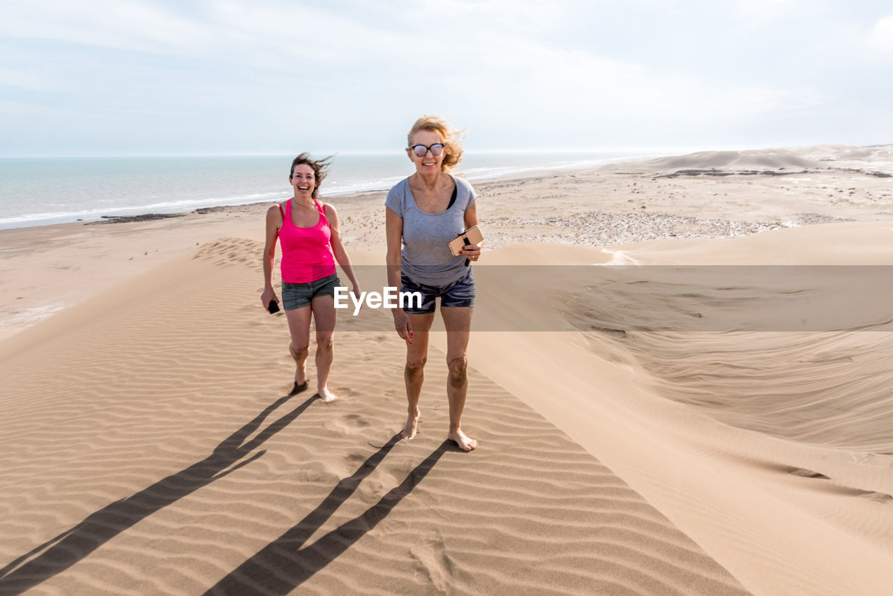 Frontal view of two women walking on top of a large dune. mother and daughter