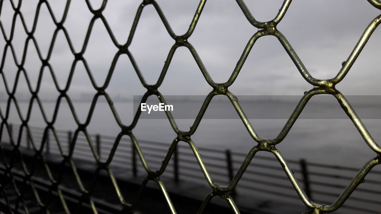 Sea seen through chainlink fence against sky