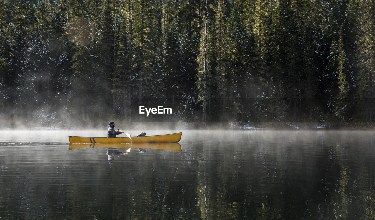 Bearded man paddles boat on calm lake with mist rising off