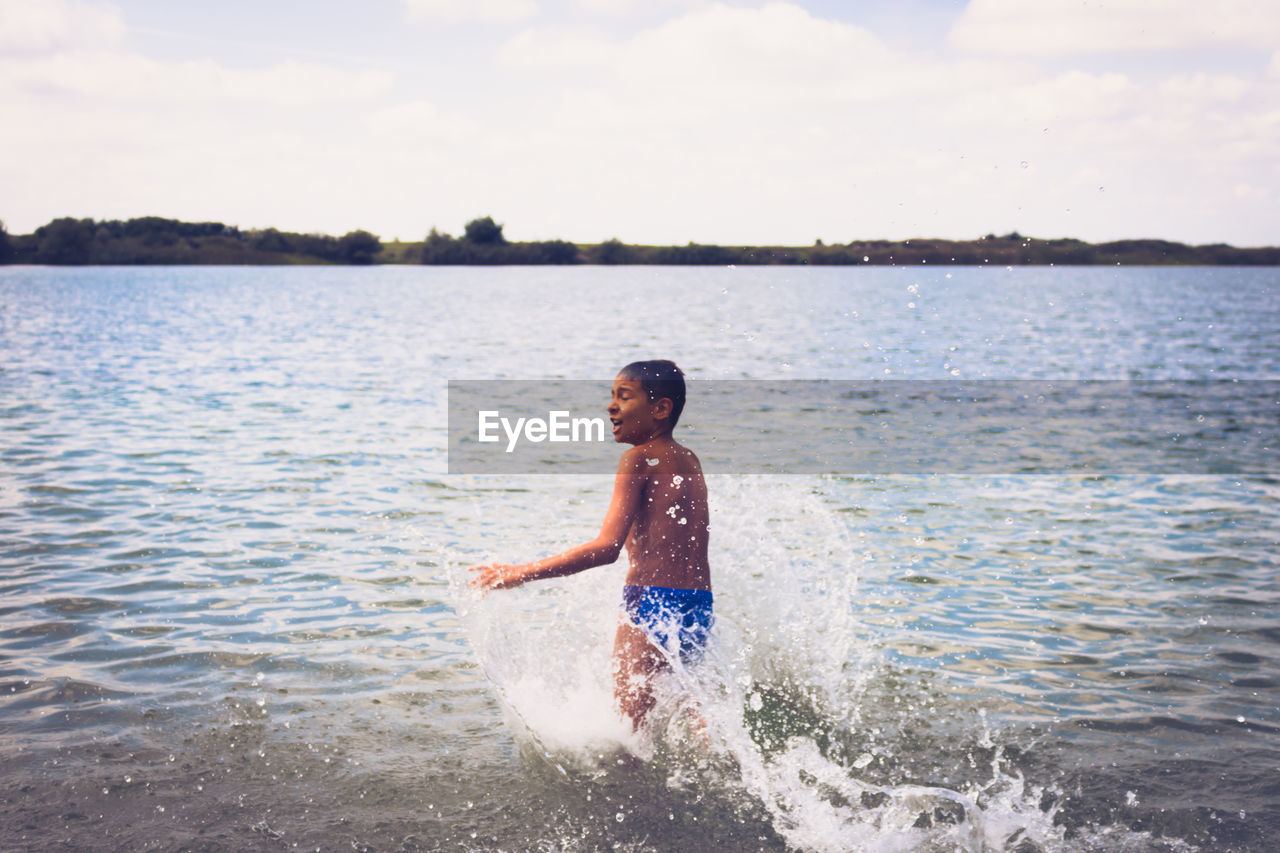 Carefree boy having fun in summer day and rushing in the water at the beach. copy space.