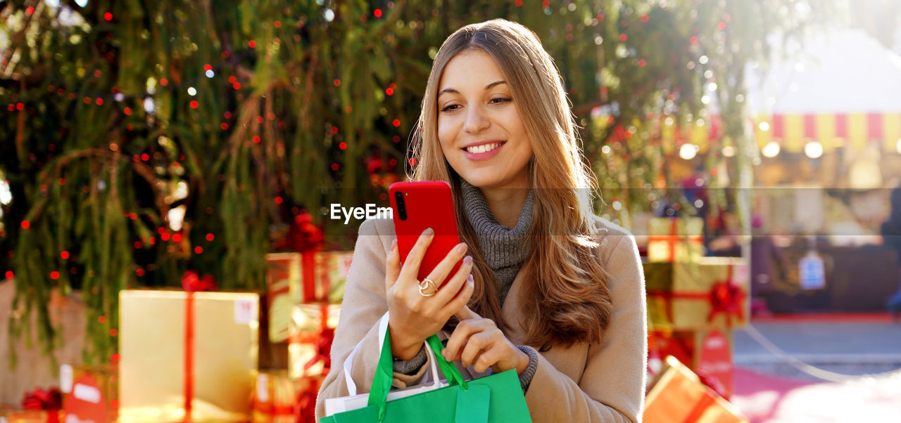 Woman receiving christmas wishes on smartphone when walking between christmas markets outdoors