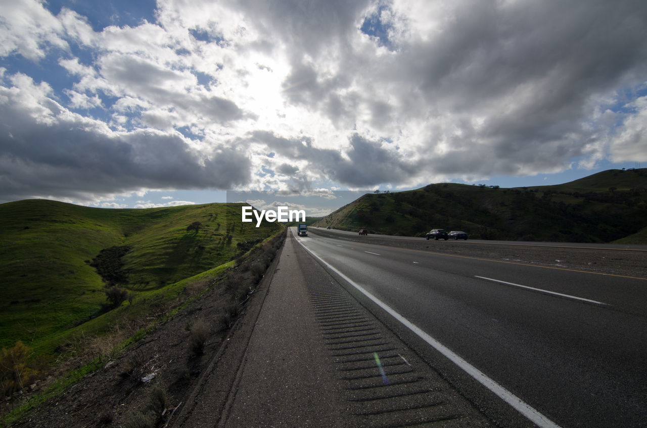 Road passing through landscape against cloudy sky