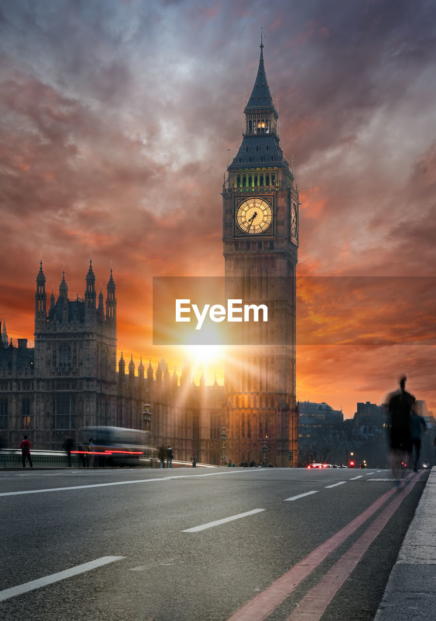 Blurred motion of vehicles on road by big ben against sky during sunset