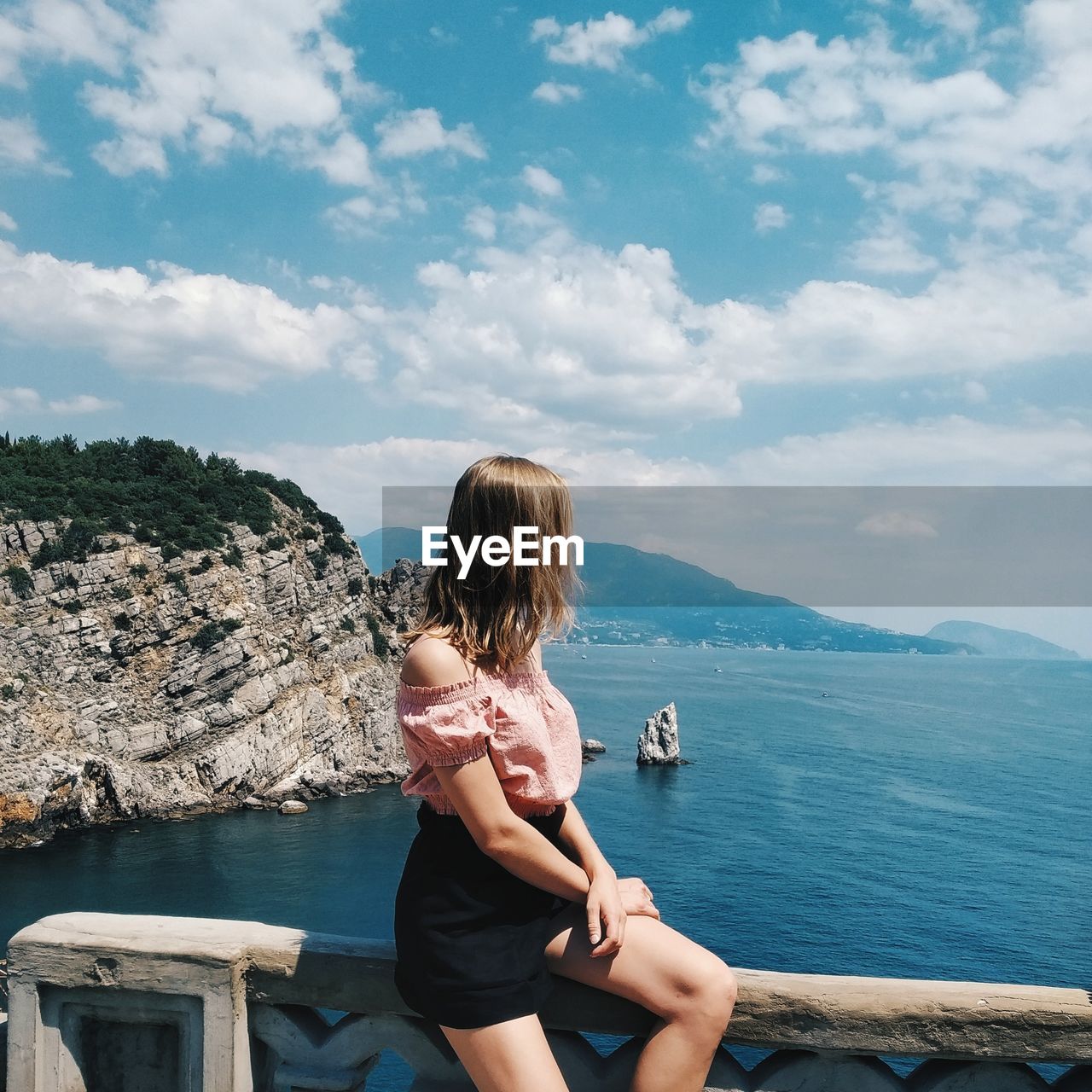 REAR VIEW OF WOMAN LOOKING AT SEA AGAINST MOUNTAIN