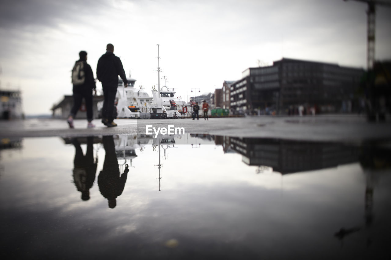 Reflection of buildings and people seen in puddle on road