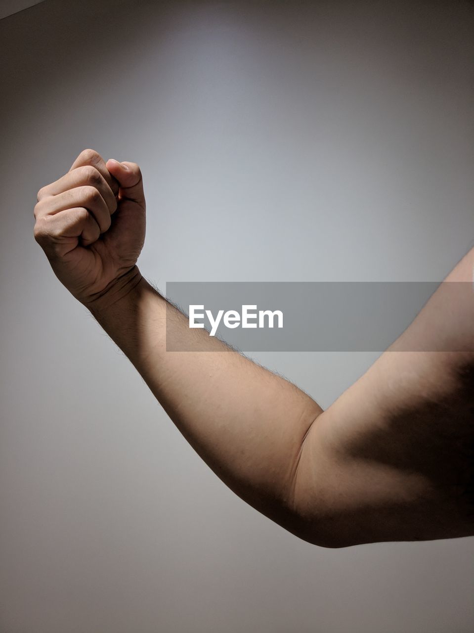 Cropped hand of man flexing muscles against white wall