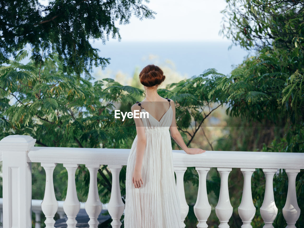 REAR VIEW OF WOMAN STANDING ON RAILING AGAINST BALCONY