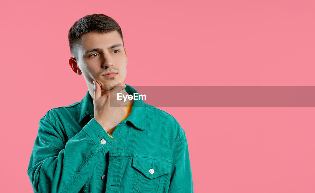 studio shot, colored background, one person, portrait, adult, indoors, copy space, young adult, looking at camera, outerwear, front view, clothing, sleeve, waist up, serious, pink background, men, contemplation, headshot, emotion, looking, person, standing, brown hair, pink, casual clothing, button down shirt, individuality, photo shoot, blue