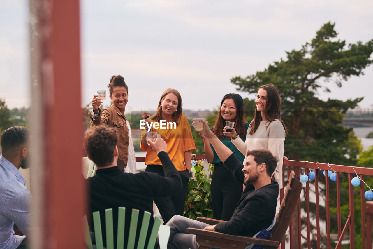 Happy friends toasting drinks on terrace during party