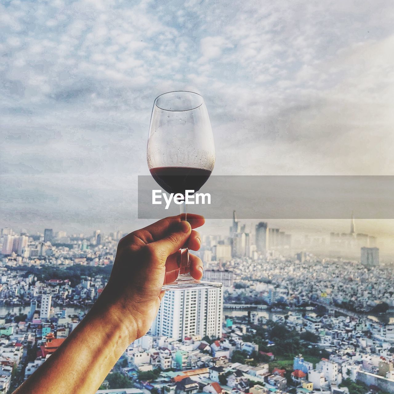 Cropped hand of man holding wineglass against cityscape