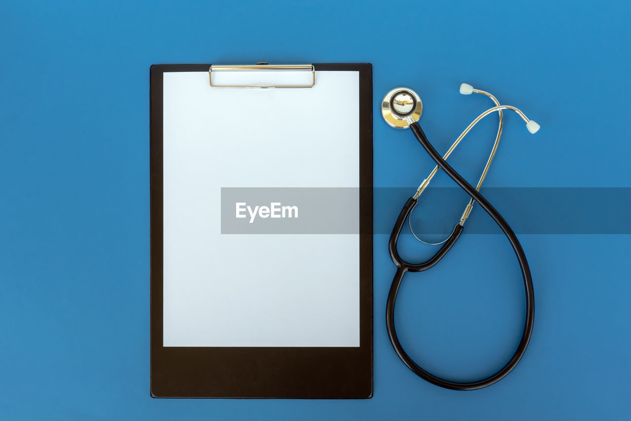 Directly above shot of clipboard with stethoscope on blue background