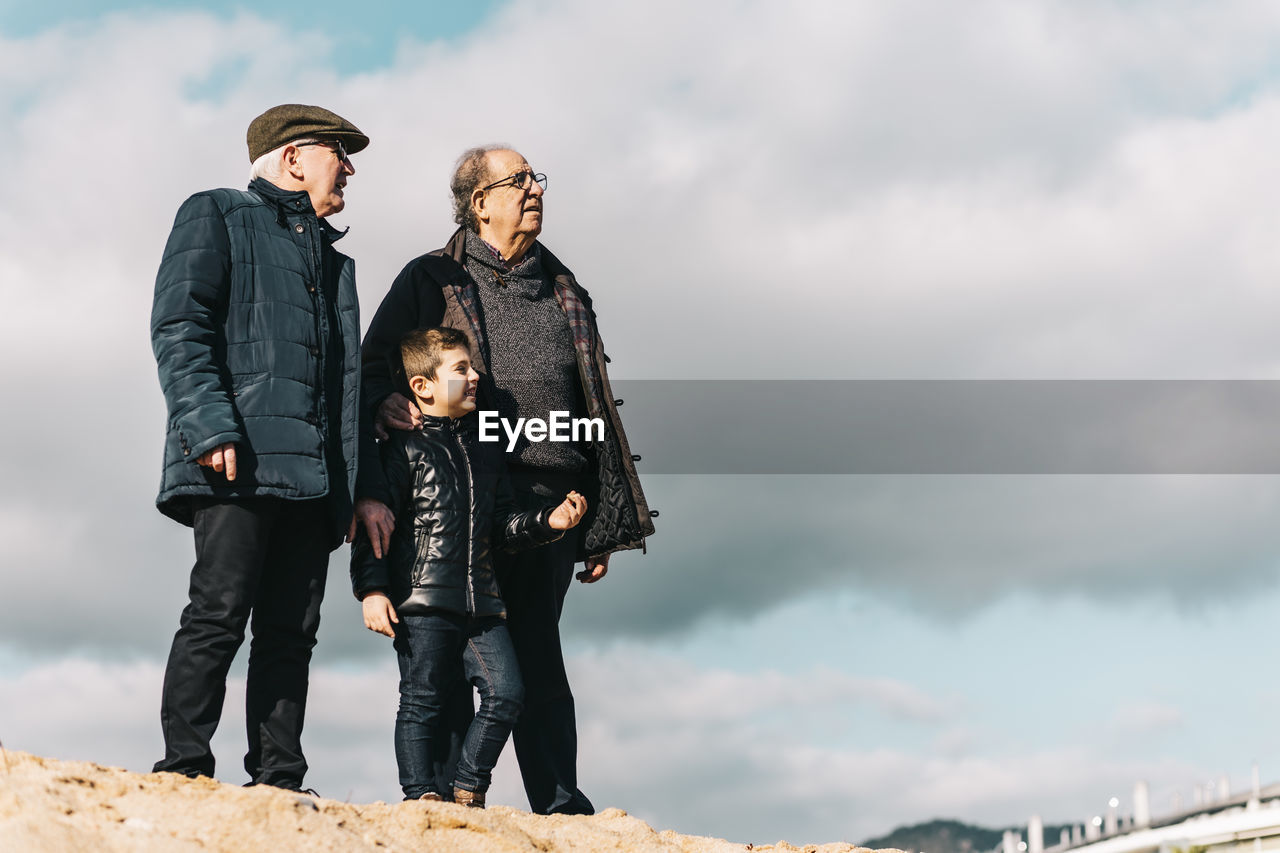 Full length of senior men with child standing against sky