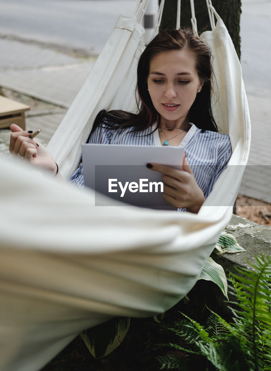 Young woman drawing on sketch pad while lying in hammock