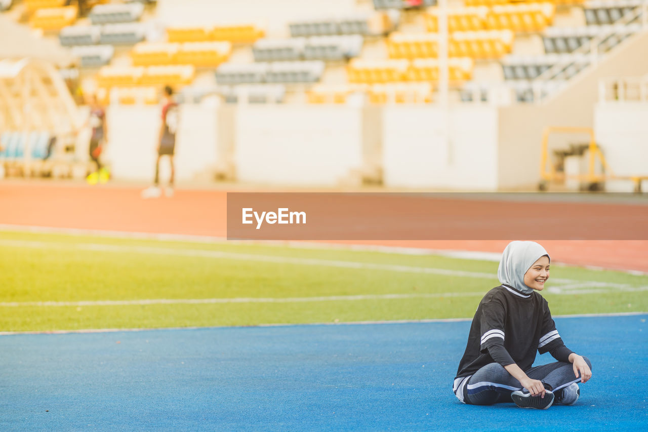 Full length of female athlete sitting at stadium