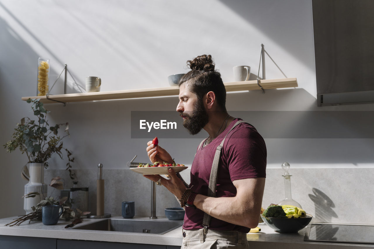 Man eating strawberry while standing in kitchen