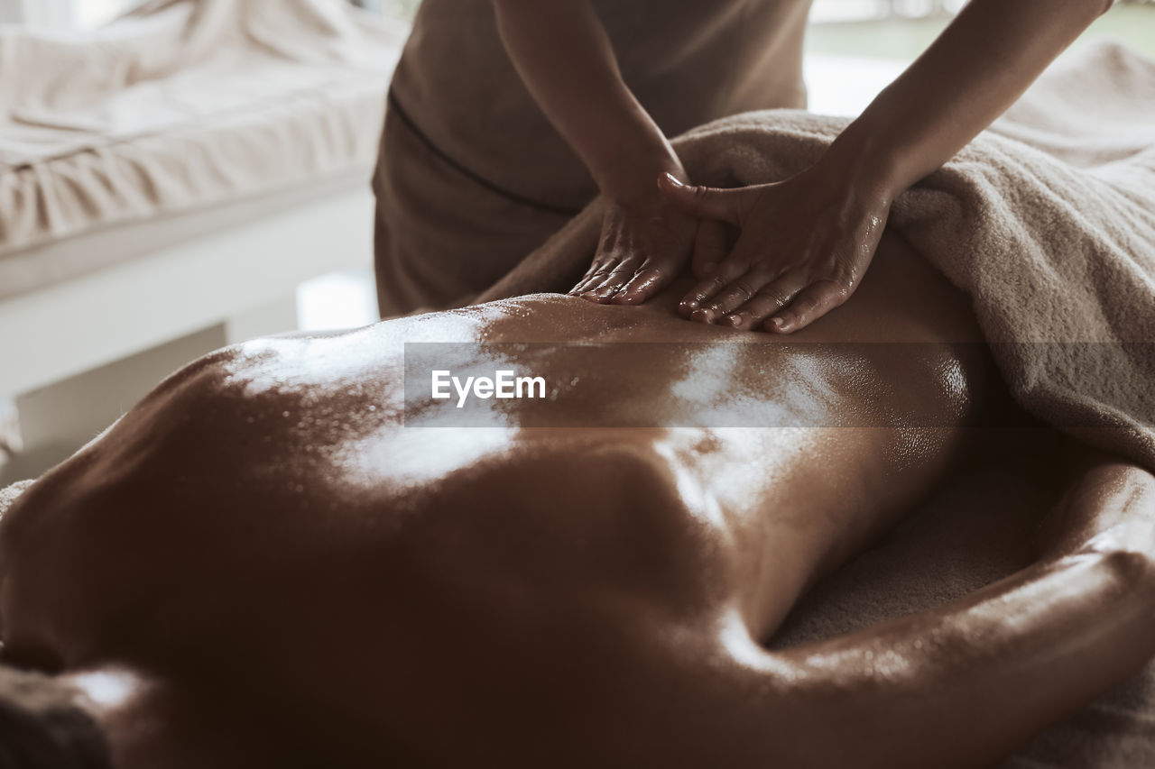 Midsection of masseuse giving massage to woman at spa