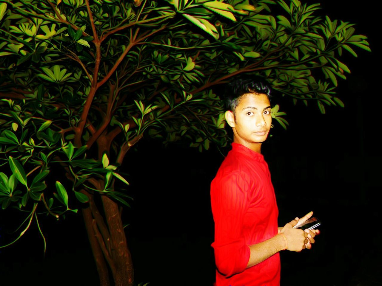 YOUNG WOMAN USING MOBILE PHONE WHILE STANDING ON TREE