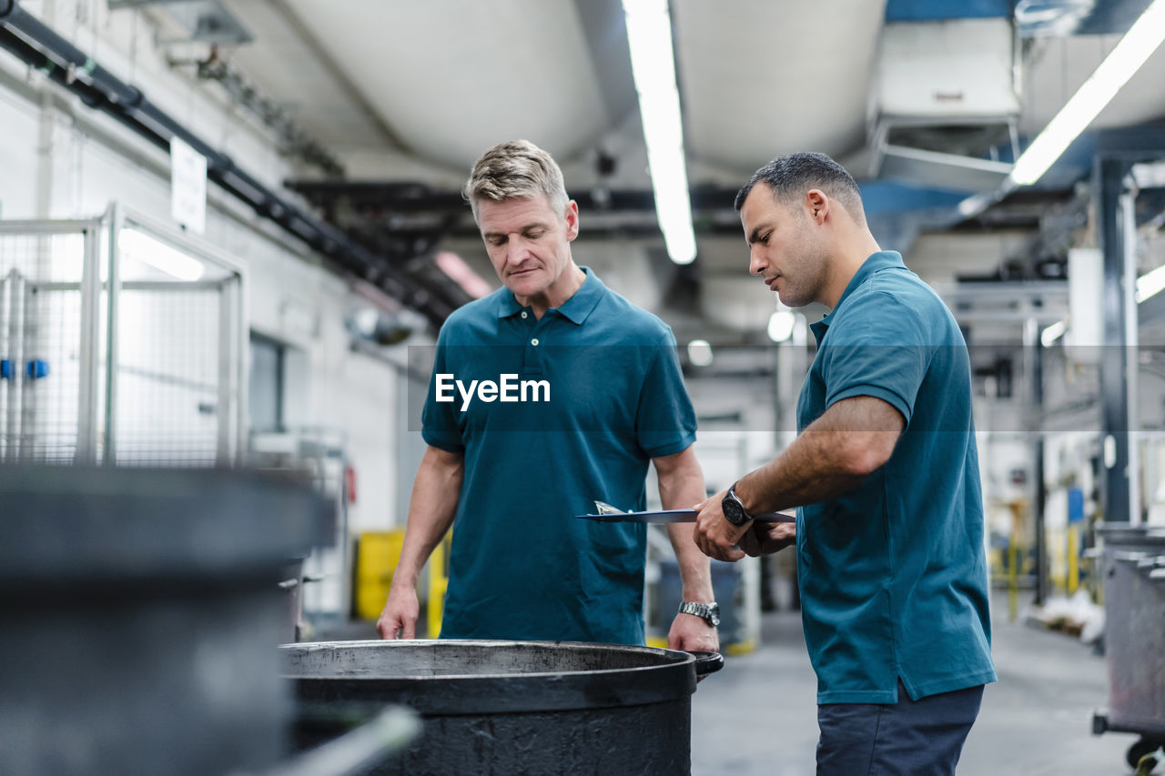 Male professionals looking into barrel while standing in factory