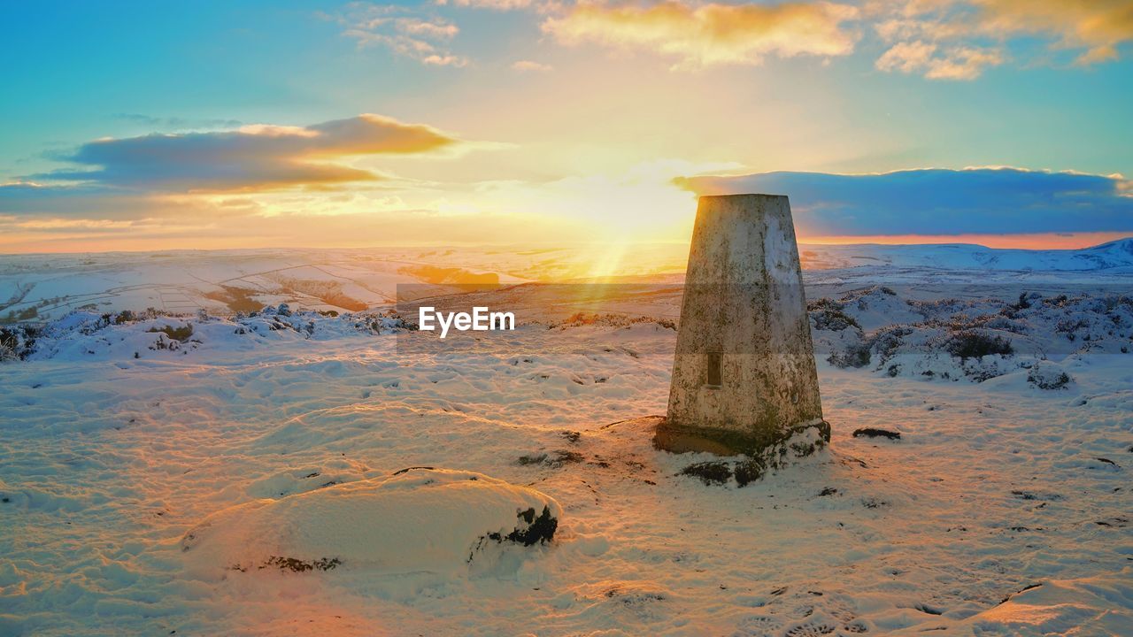 WOODEN POSTS ON SNOW COVERED LAND DURING SUNSET