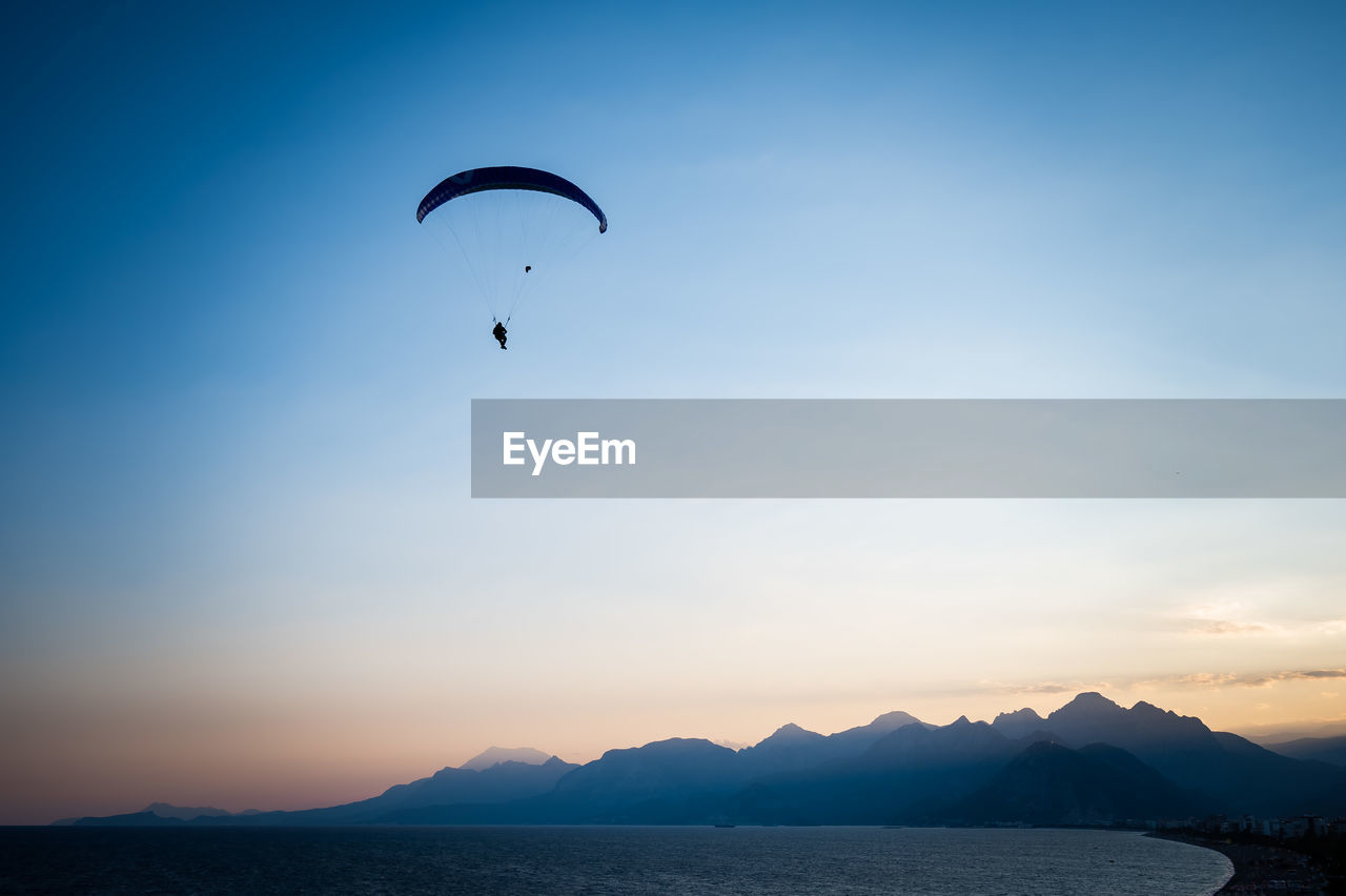 low angle view of people paragliding over sea against sky during sunset