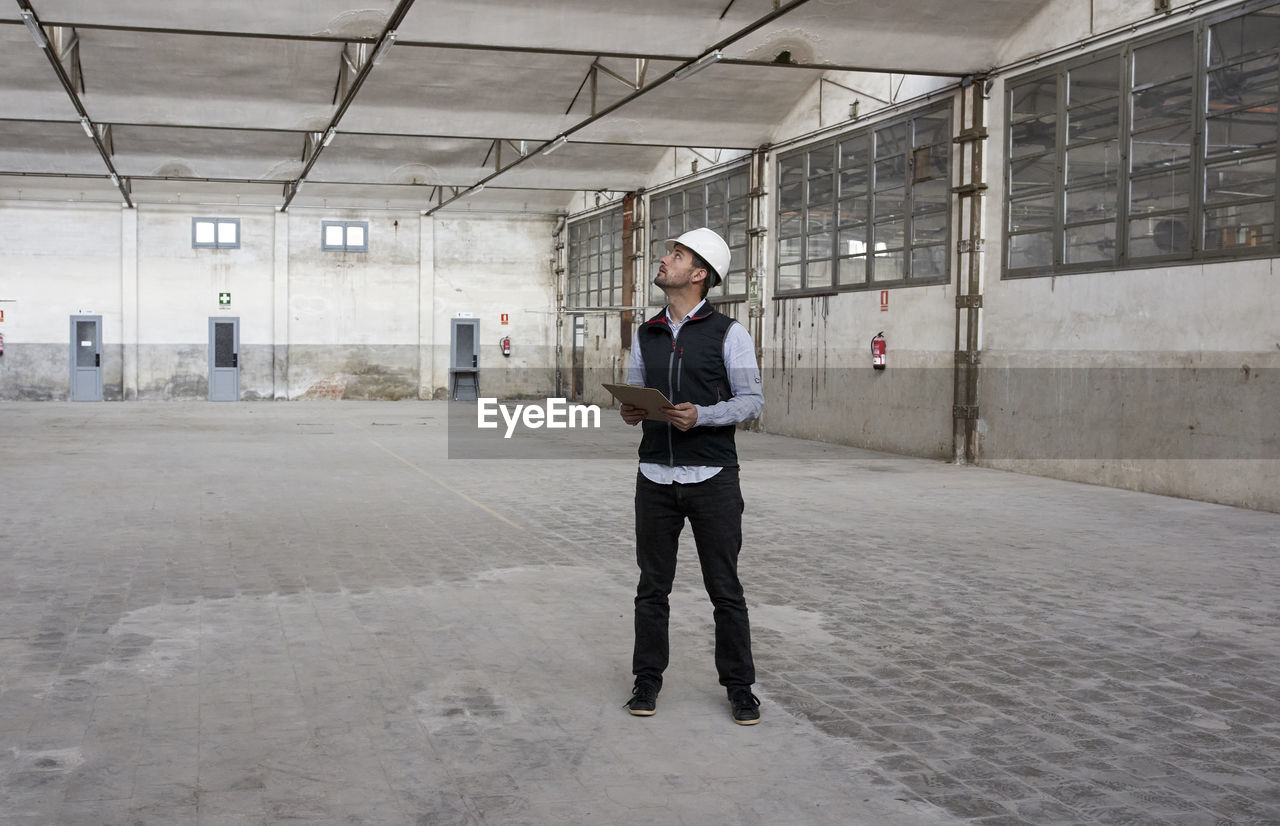 Male architect with map looking up while standing in constructing building