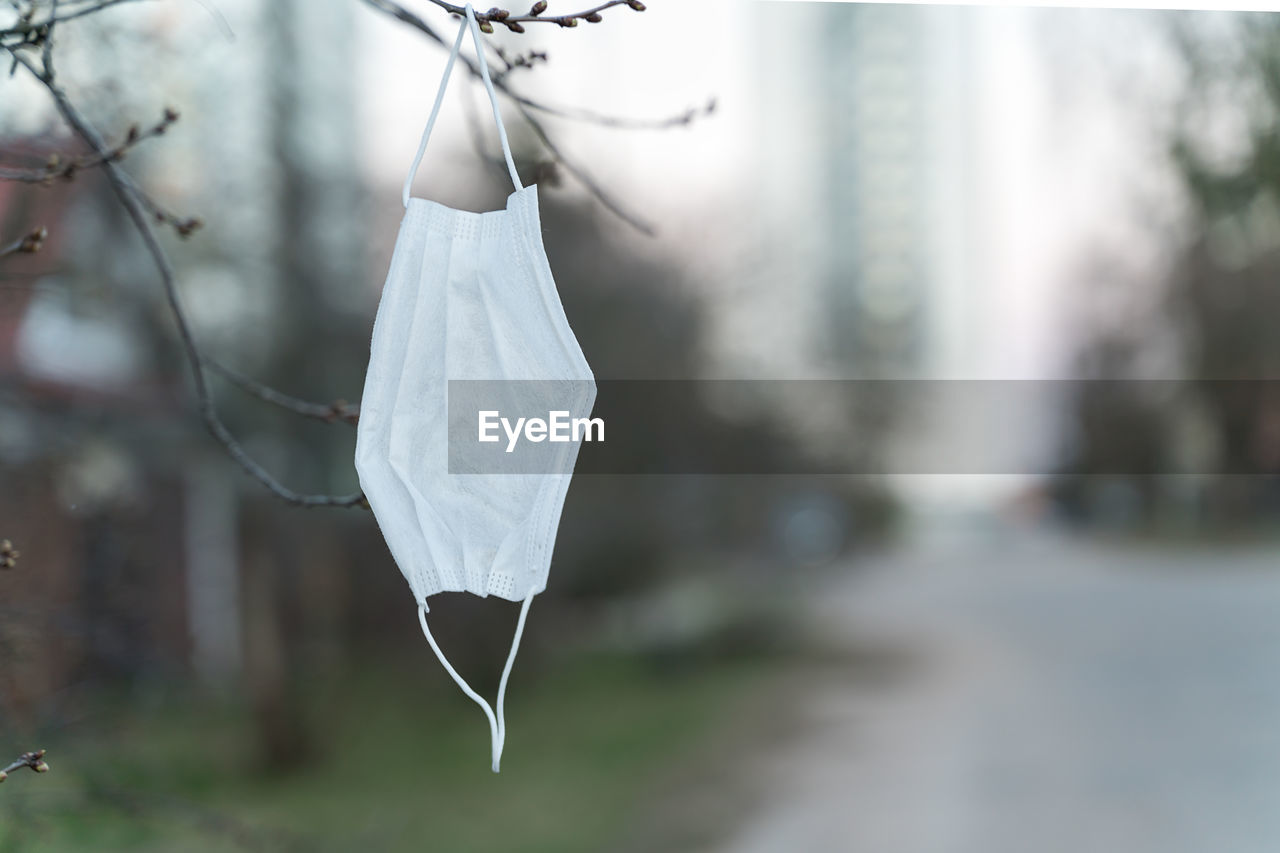 Disposable white surgical mask hanging on a tree branch