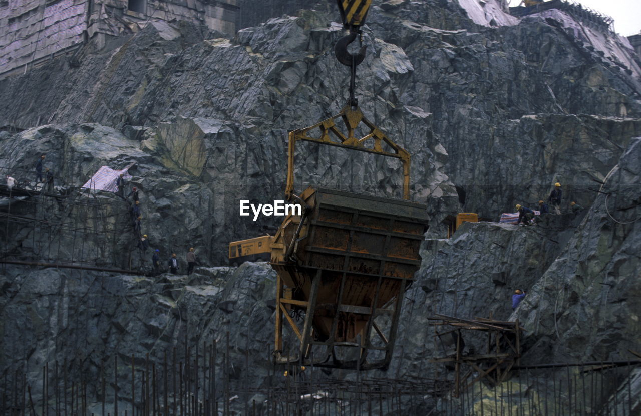 Low angle view of crane against rocky mountains at construction site