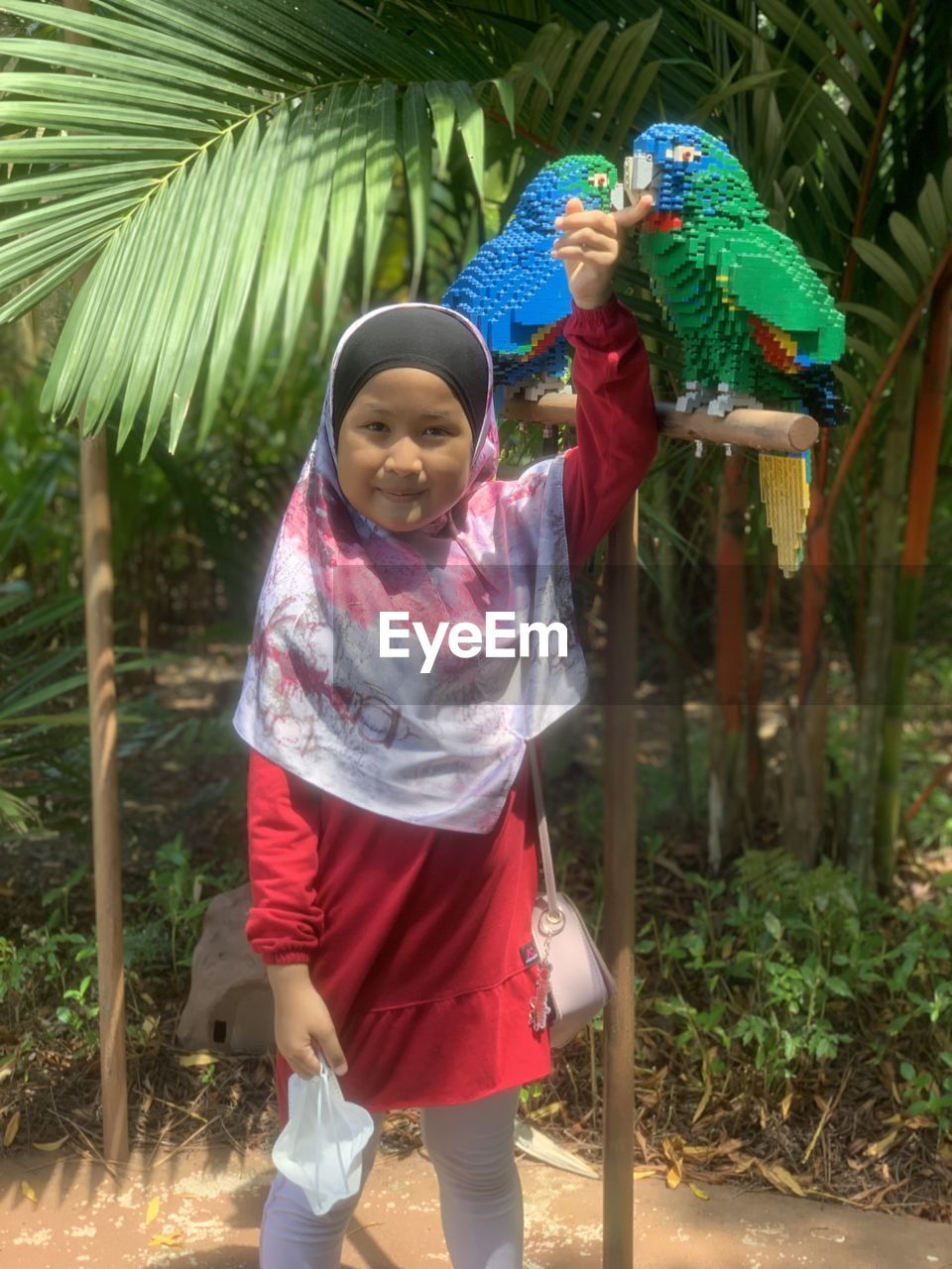 child, childhood, women, female, full length, nature, smiling, clothing, day, standing, one person, plant, lifestyles, tree, looking at camera, front view, happiness, portrait, traditional clothing, adult, person, outdoors, leisure activity, men, tropical climate, emotion, holding, human face, casual clothing, palm tree, tradition, flower